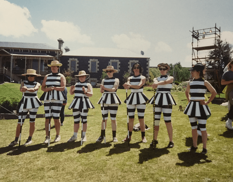 A group of people, dressed in a black and white striped outfits while holding canes.