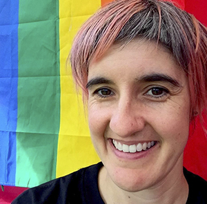 A woman smiling while standing in front of a rainbow background.