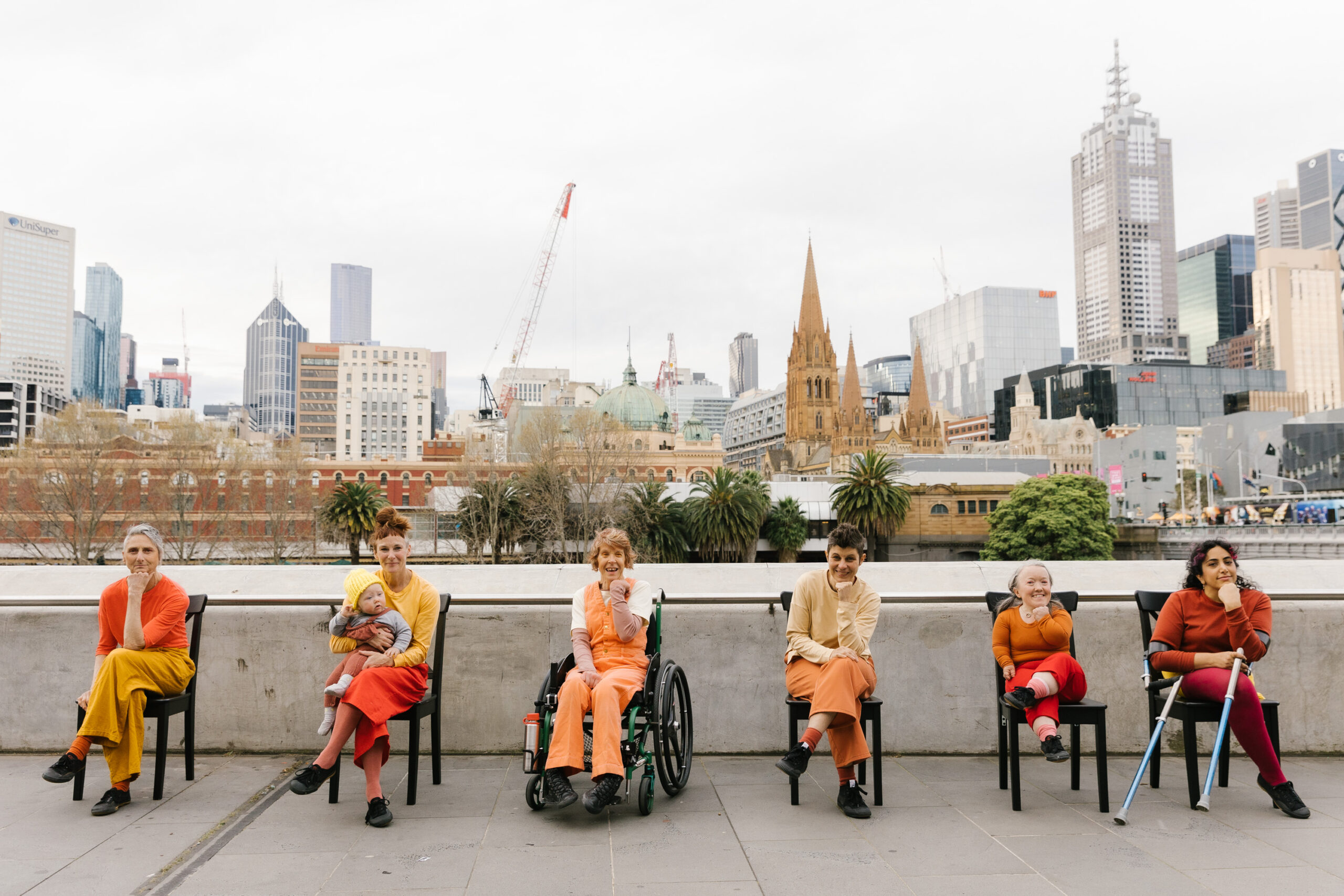 Momentum cast sitting in chairs posing in front of Melbourne city. Credit Kate Disher-Quill